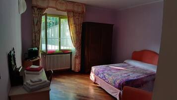 Ein Schlafzimmer mit Bett, Schminktisch, Spiegel, Heizkörper und einem Fenster mit Vorhängen.