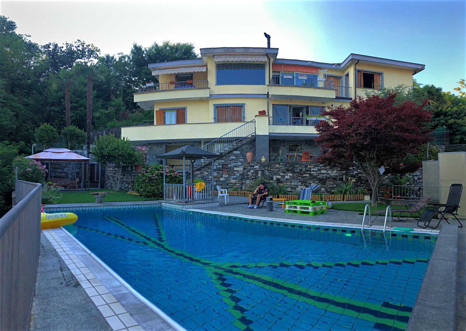 A two-story building with a swimming pool, a covered patio, and a stone wall.