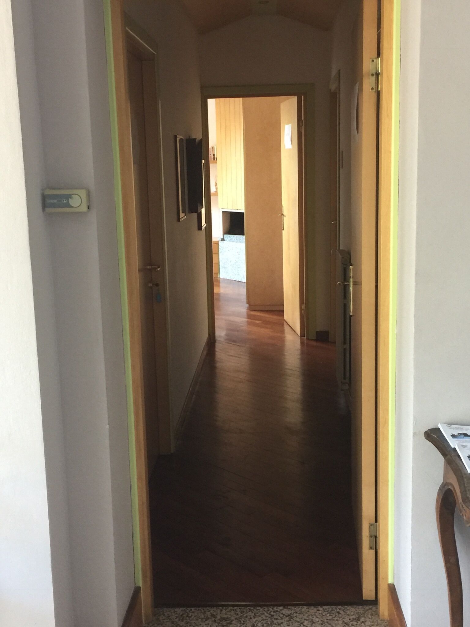 Un pasillo estrecho con suelo de madera y una puerta a la derecha.