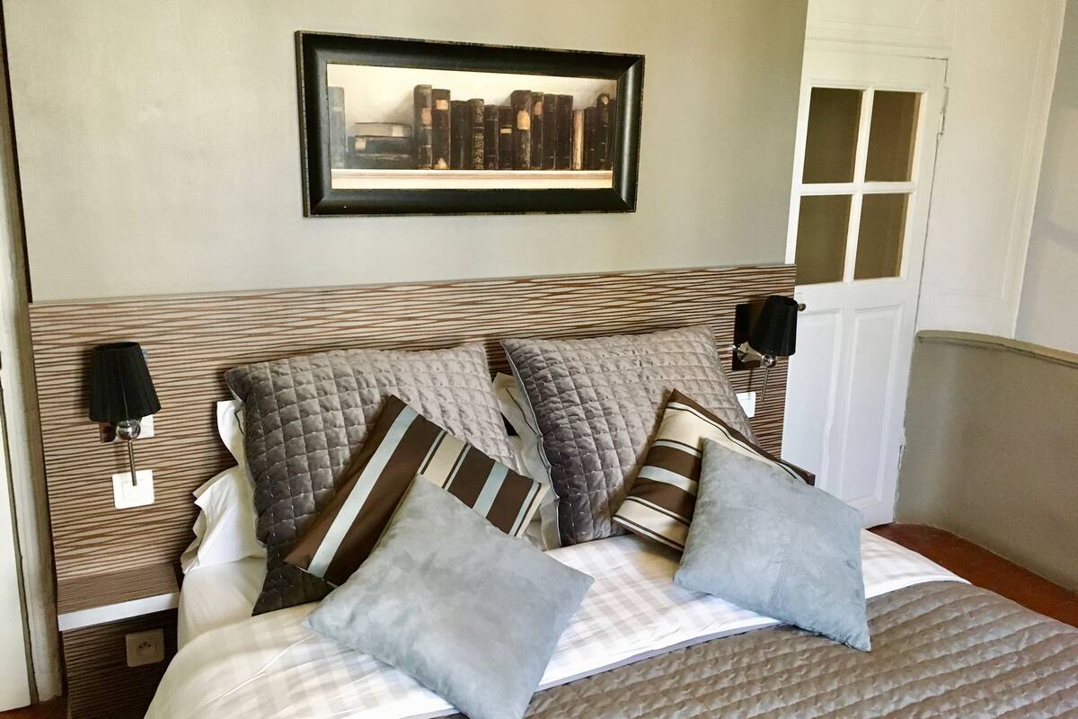 A neatly made bed with multiple pillows and a framed picture above it.