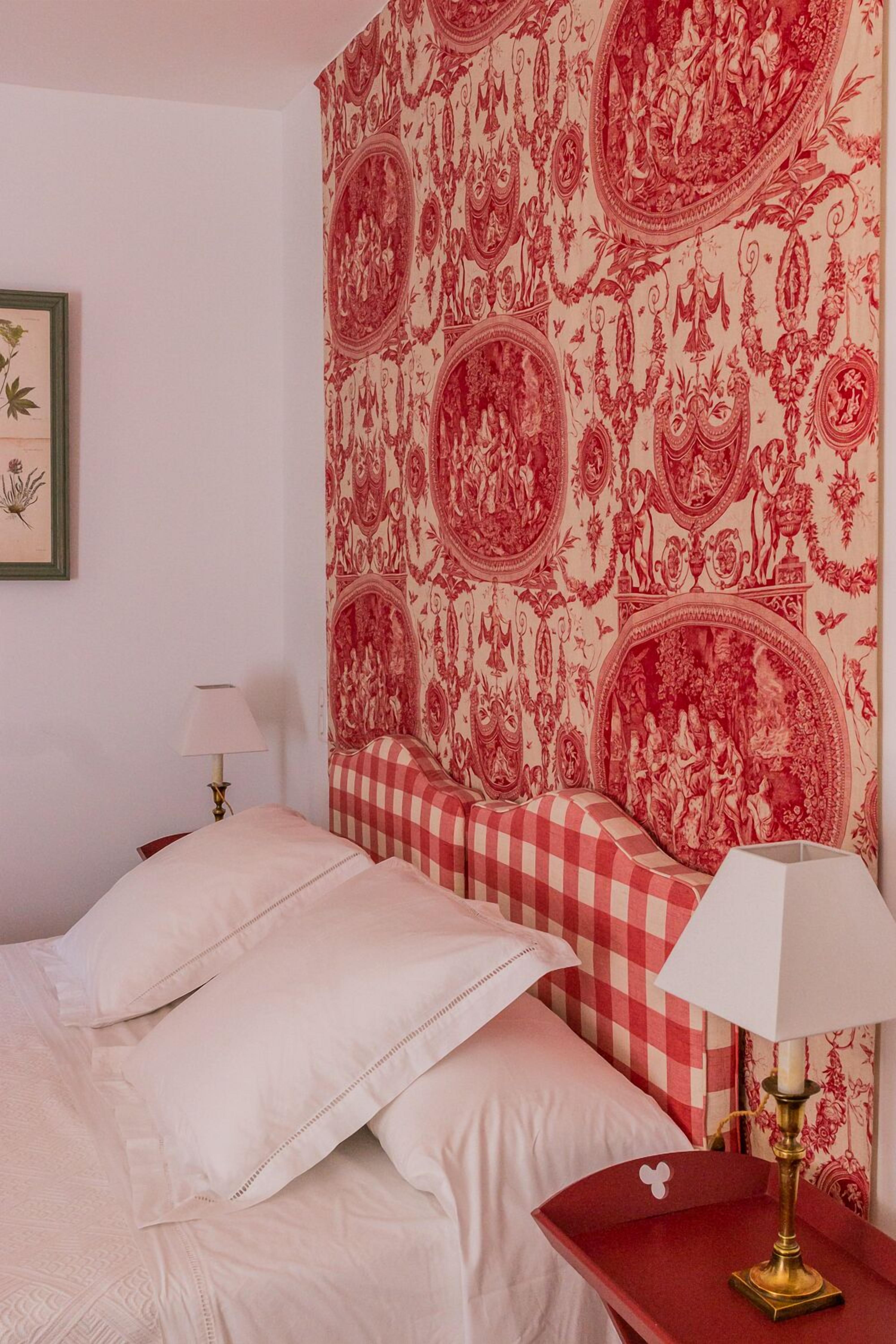 A bedroom with a checkered headboard, a bedside table with a lamp, and a wall tapestry.