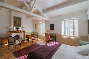 Una habitación amplia con una cama grande, una silla de madera, una mesita pequeña y una chimenea.