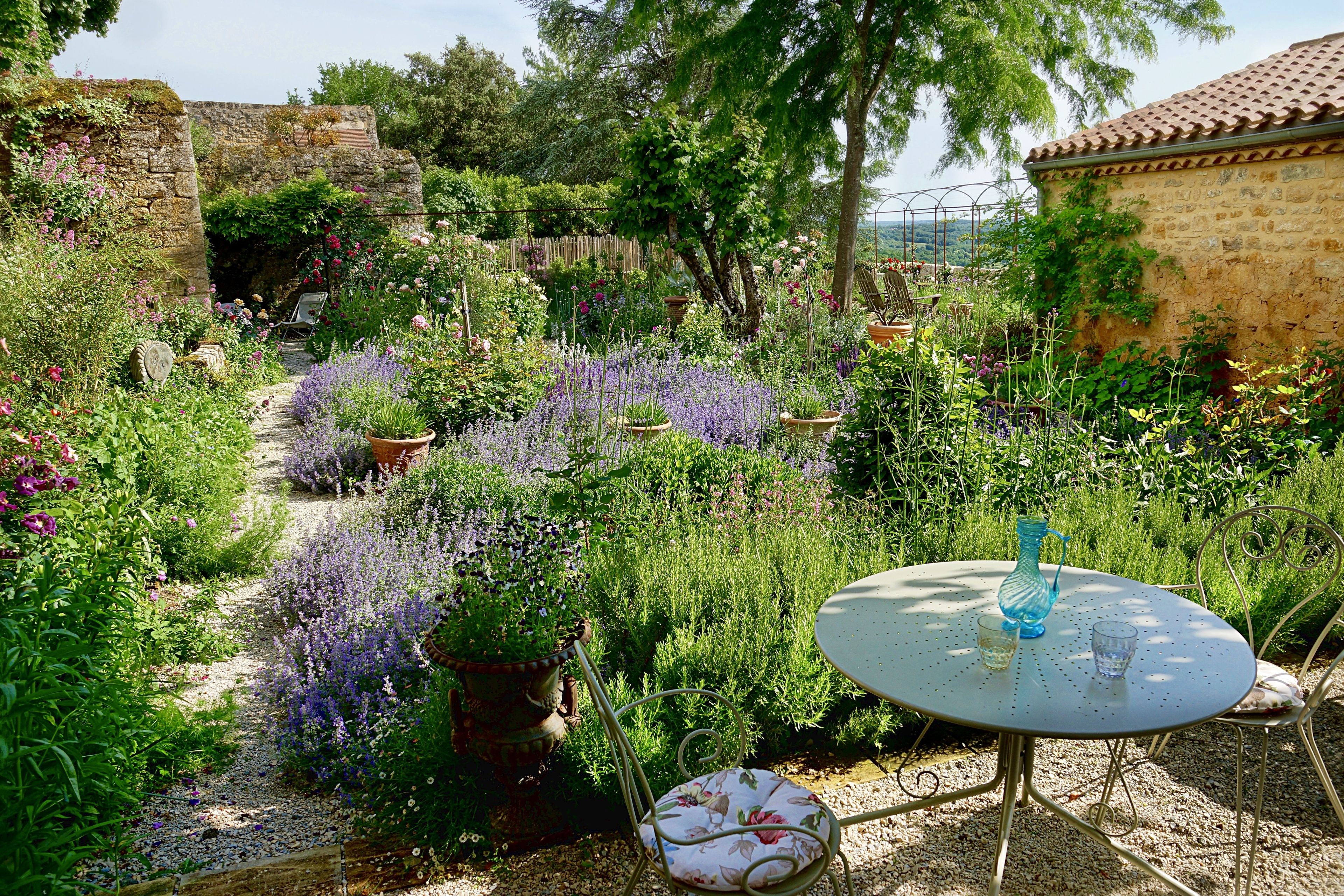 Um jardim com mesa e cadeiras, cercado por diversas plantas e flores.