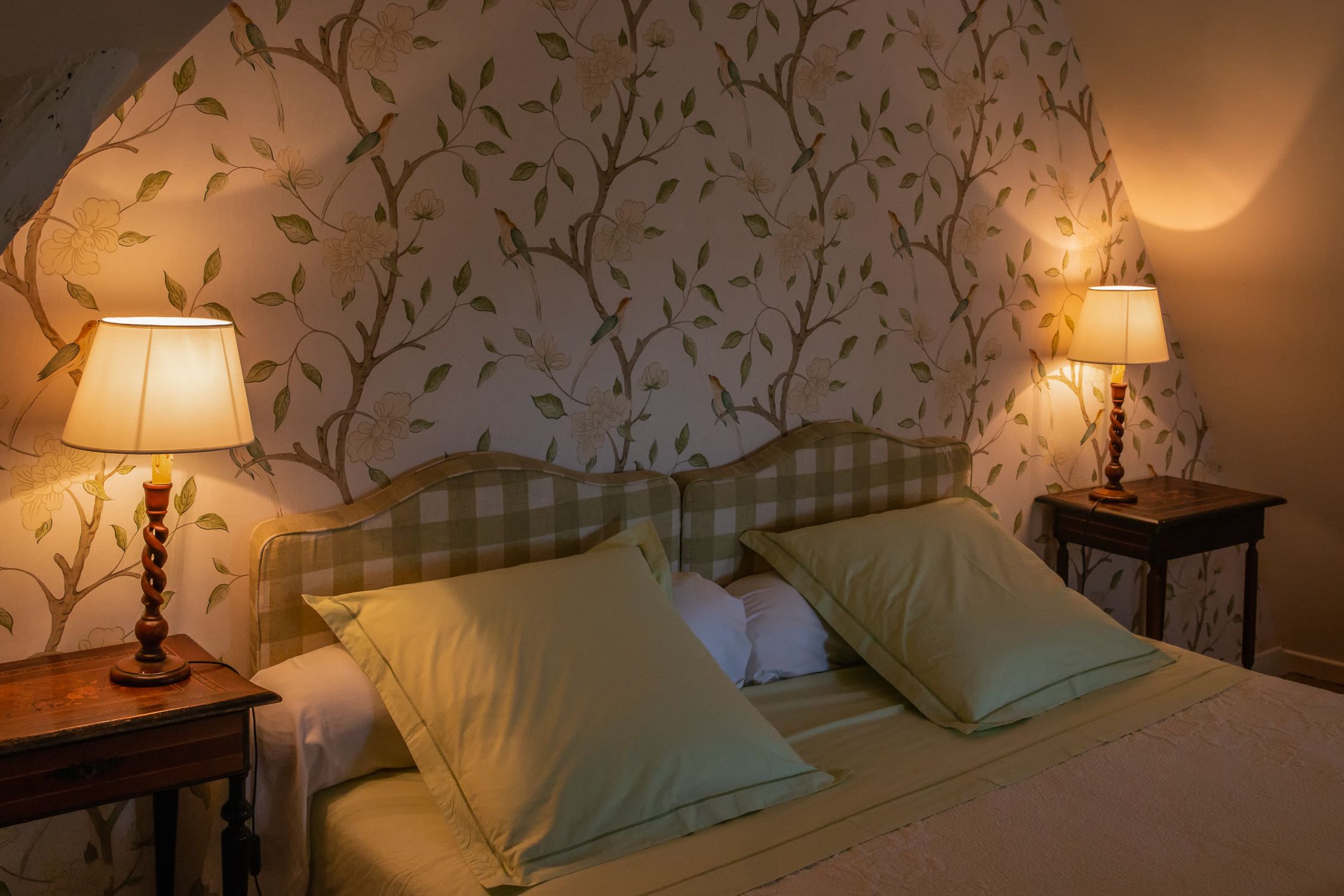 A bedroom with a checkered headboard, two bedside tables with lamps, and floral wallpaper.