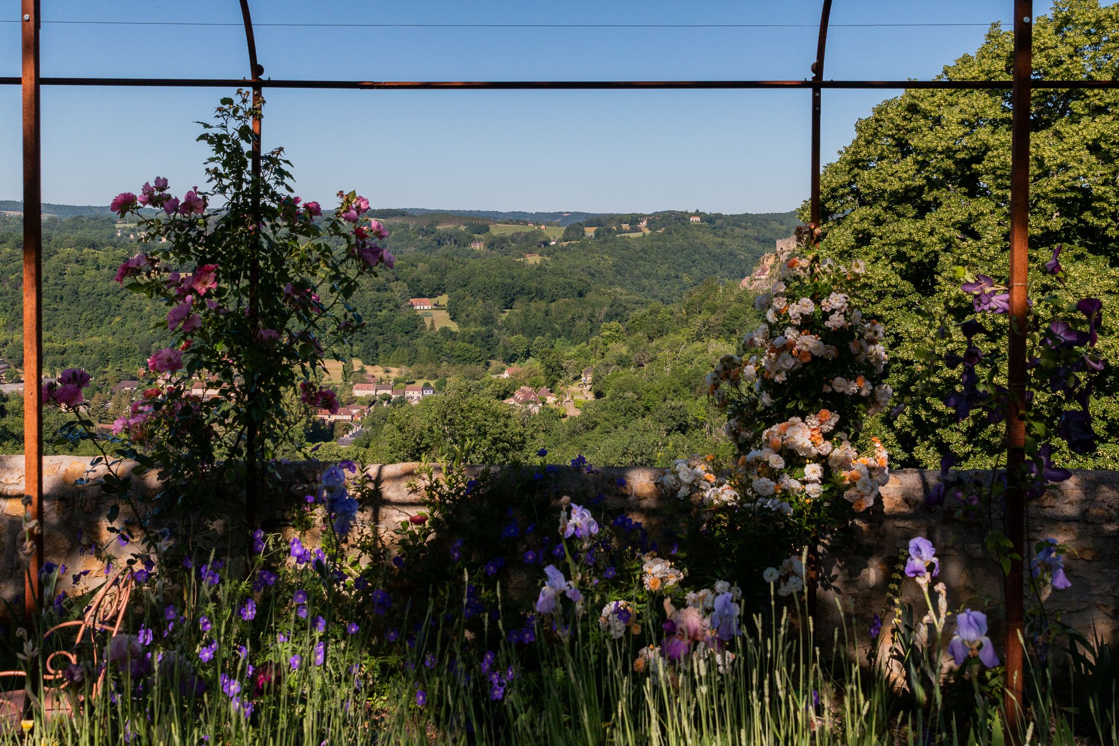 Jardín con vista a un valle, con flores moradas y blancas y un muro de piedra.