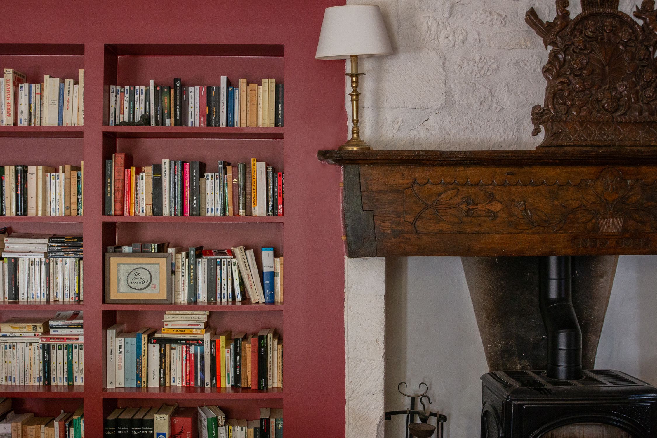 A room with a bookshelf filled with books, a fireplace with a wood-burning stove, and a white lamp.