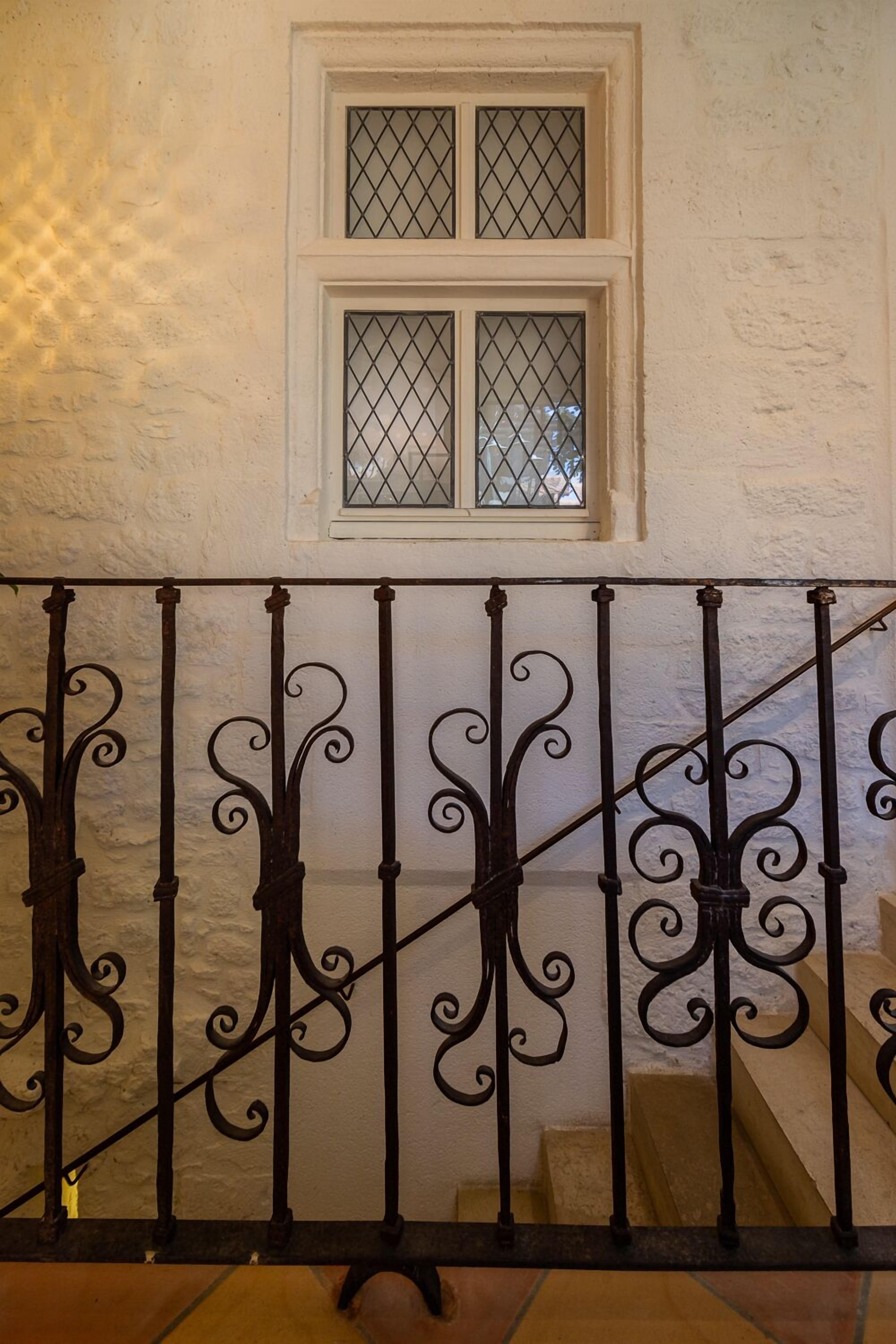 A staircase with ornate black metal railings and a window with a diamond-patterned glass.