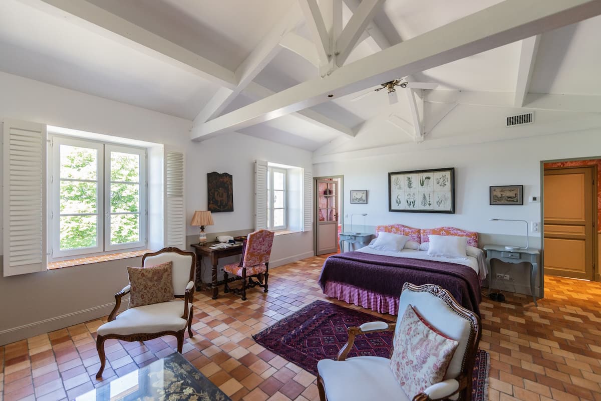 Un dormitorio con una cama grande, un escritorio, dos sillas y una ventana con contraventanas.