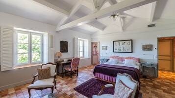 A bedroom with a large bed, a desk, two chairs, and a window with shutters.
