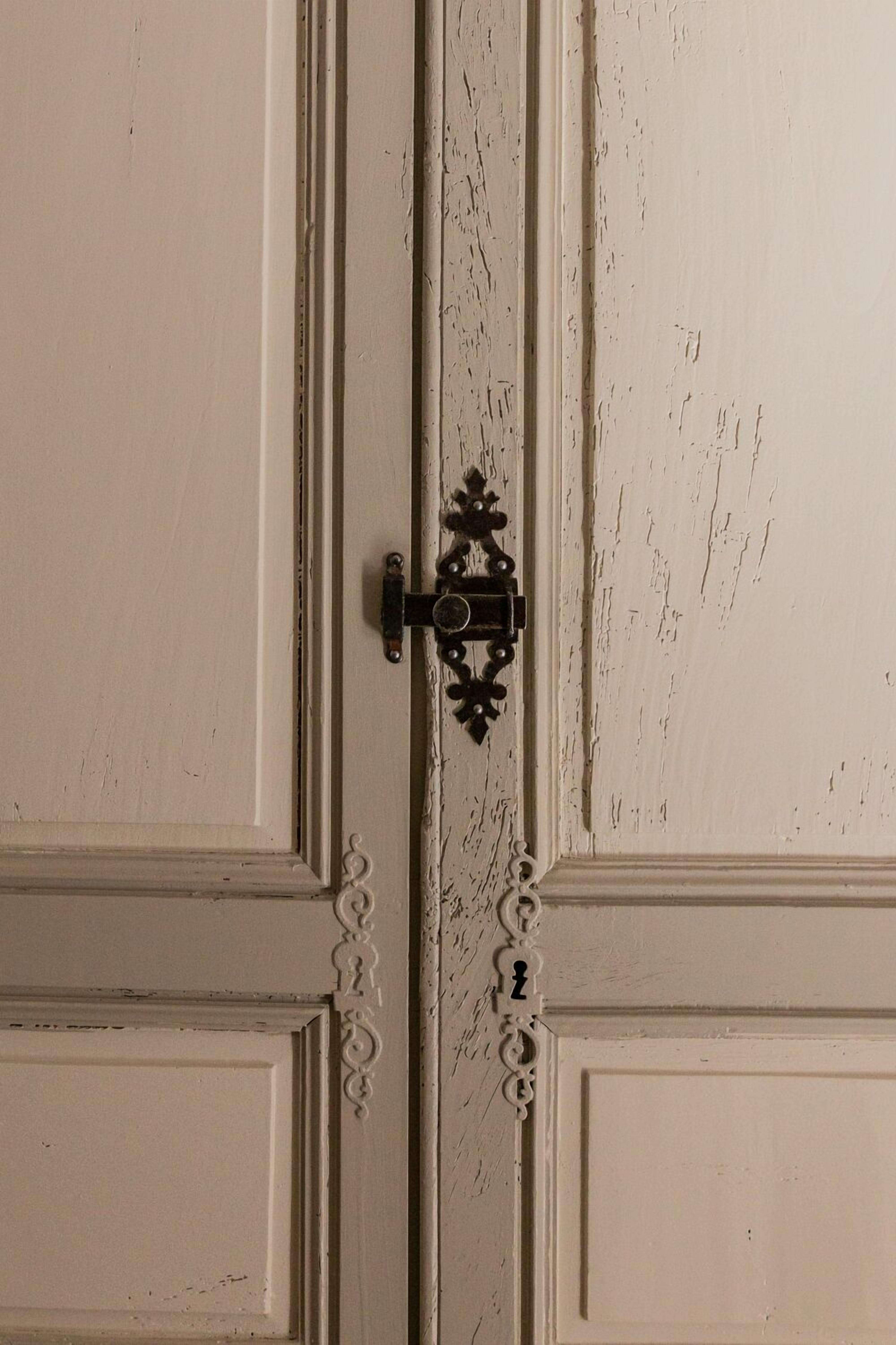 Een witte deur met een decoratieve metalen grendel en een sleutelgat.
