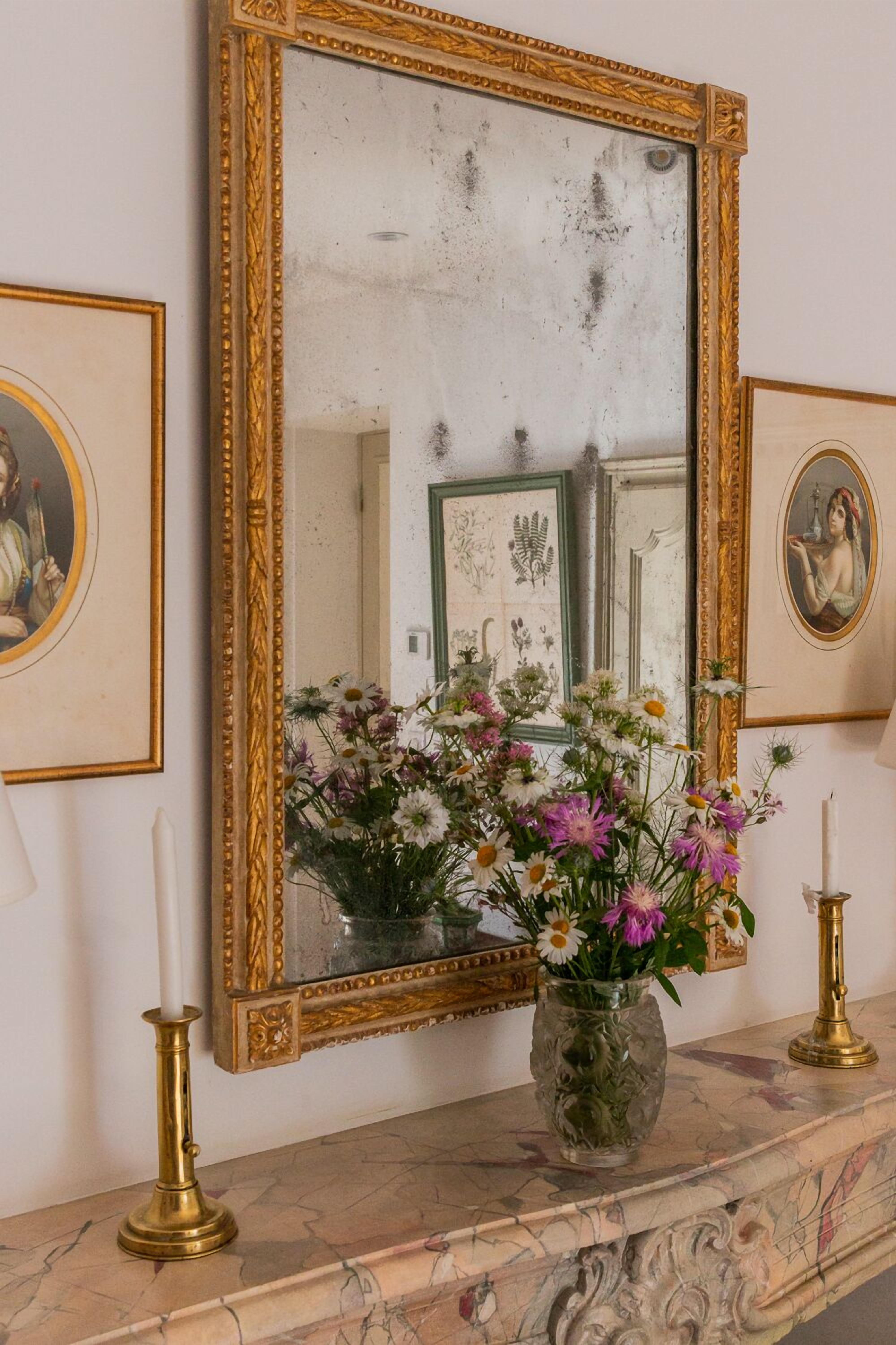 Una chimenea de mármol con un espejo de marco dorado, un florero y dos candelabros.