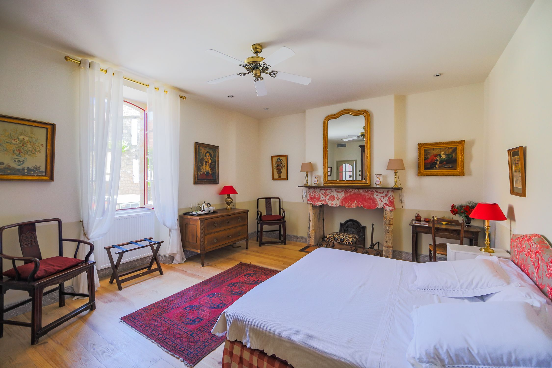 Um quarto com uma cama grande, uma cômoda de madeira, uma cadeira, uma escrivaninha, uma lareira e um ventilador de teto.