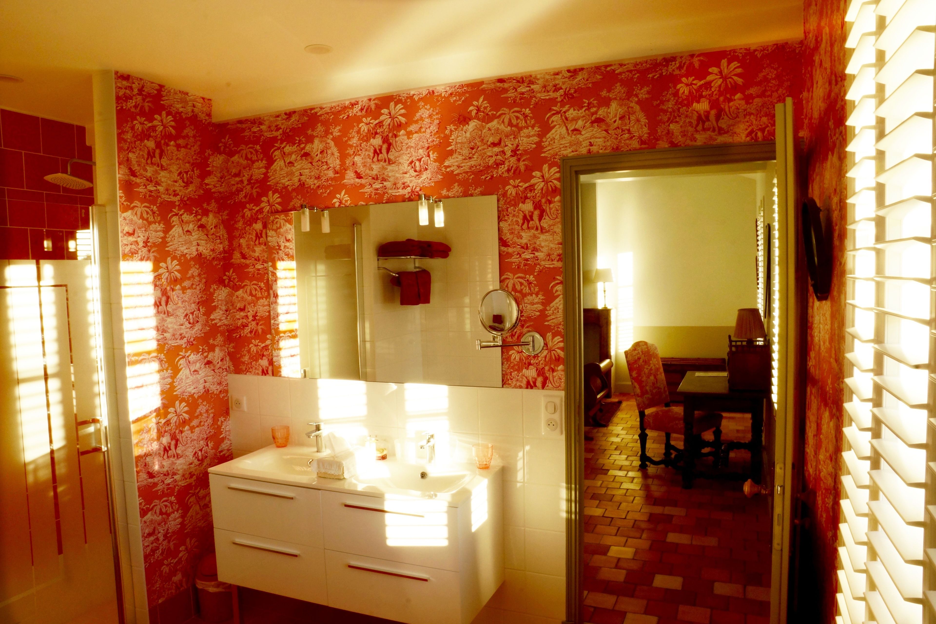 A bathroom with a white vanity, a large mirror, and a red floral wallpaper.
