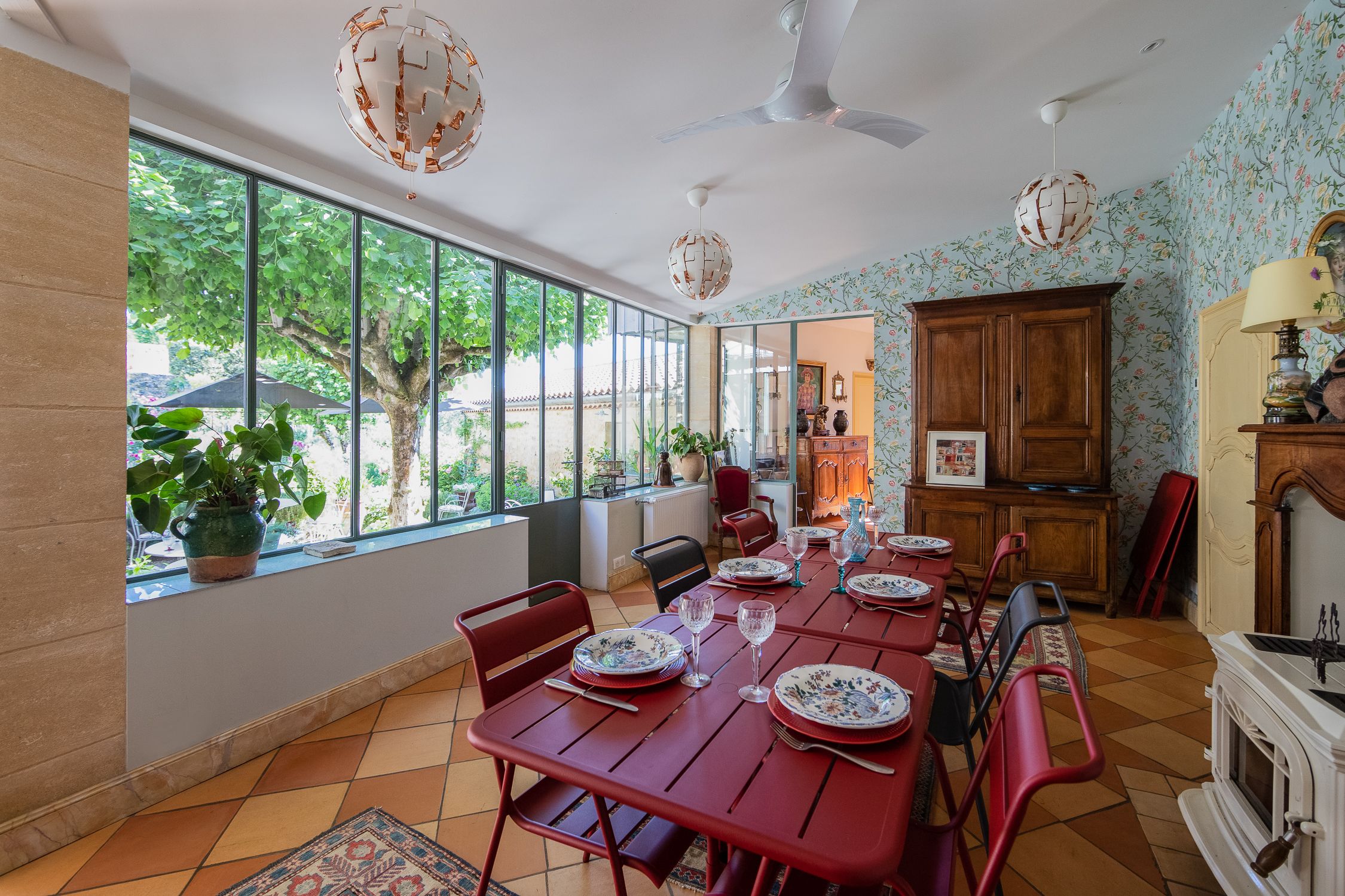 A dining area with a long table set for six, red chairs, a wooden cabinet, and a fireplace.