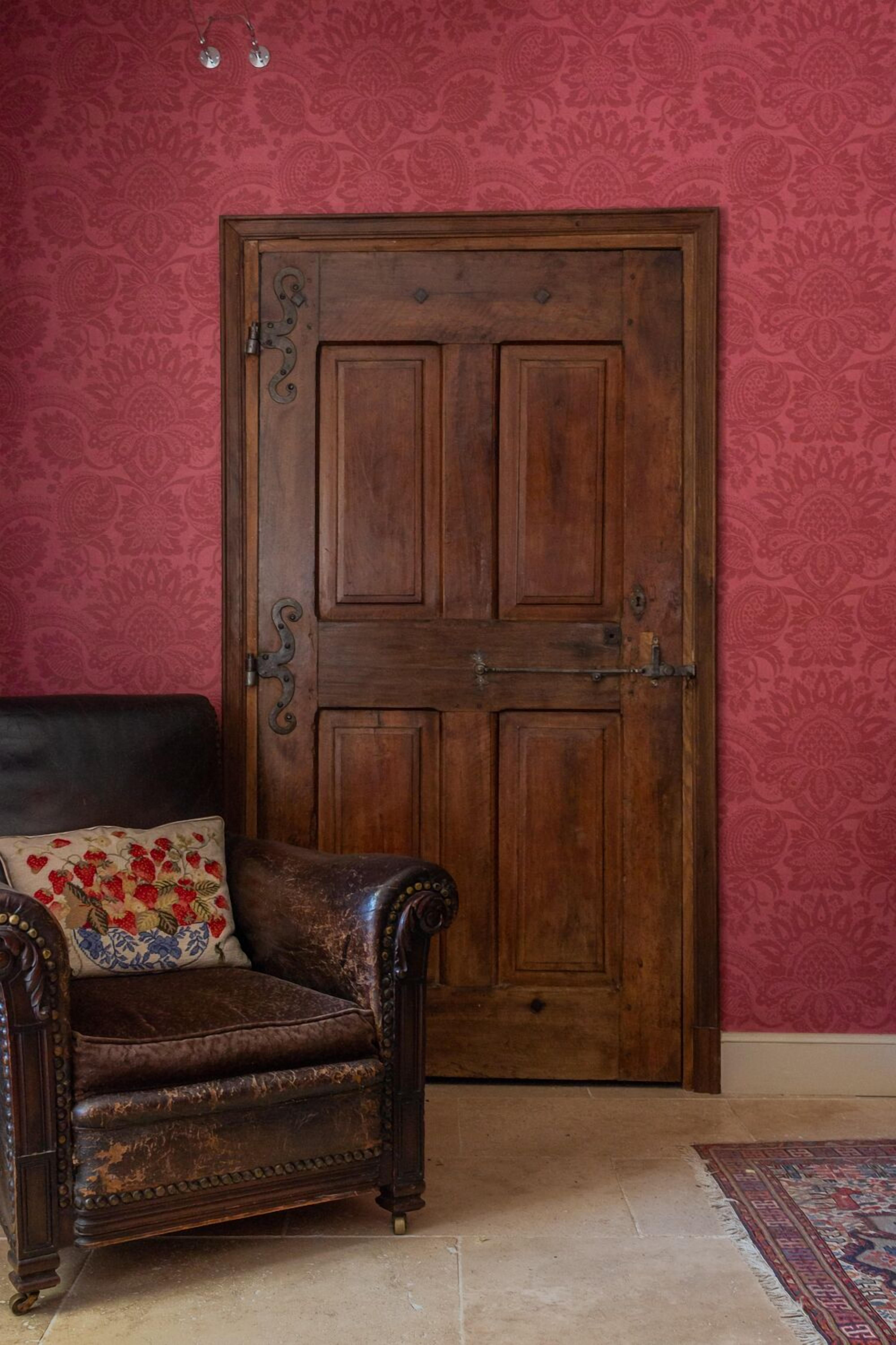 Una puerta de madera con manija de latón y un sillón de cuero marrón oscuro con un cojín estampado.