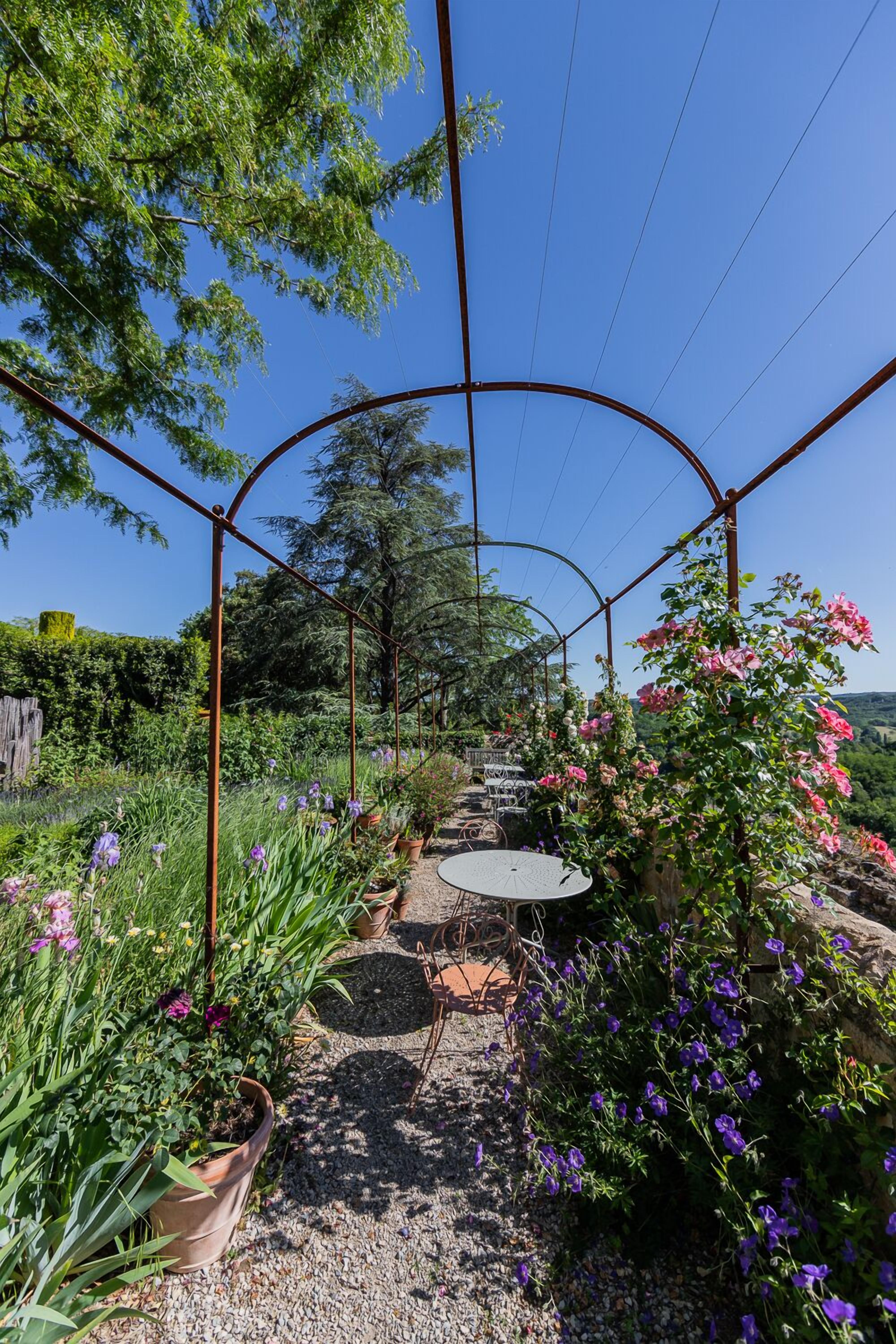 Un jardín con una estructura de pérgola, una mesa y diversas plantas.
