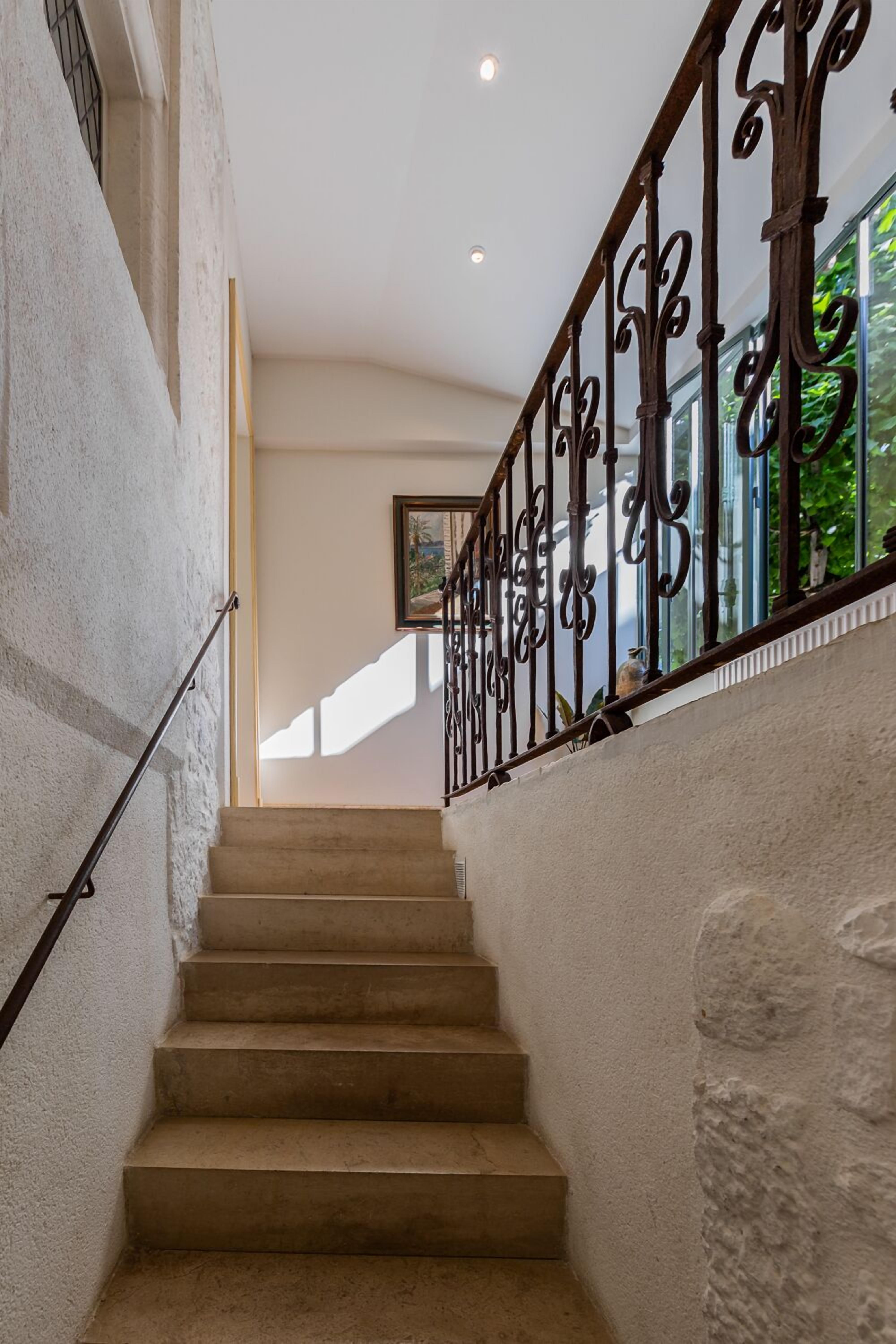 Una escalera con barandilla de metal, peldaños color beige y una pared de piedra.