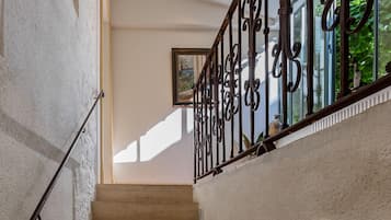 Una escalera con barandilla de metal, peldaños color beige y una pared de piedra.