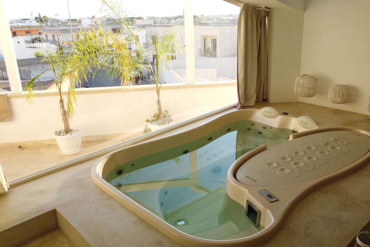 A modern bathroom with a glass-enclosed jacuzzi, potted plants, and a view of the cityscape.