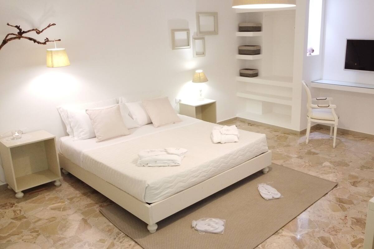 A neatly arranged bedroom with a bed, bedside tables, a desk, and a chair.