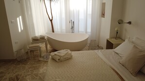 A modern bathroom with a freestanding bathtub, a small vanity with a mirror, and a bed with a quilted duvet. - Dimora TerraNostra & Spa (Ugento)
