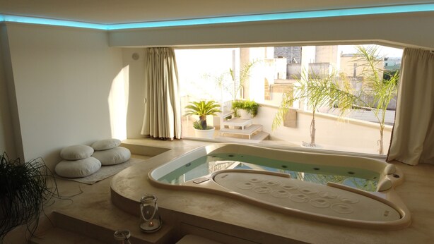 A modern bathroom with a bathtub, a small table with a candle, and a window with curtains. - Dimora TerraNostra & Spa (Ugento)