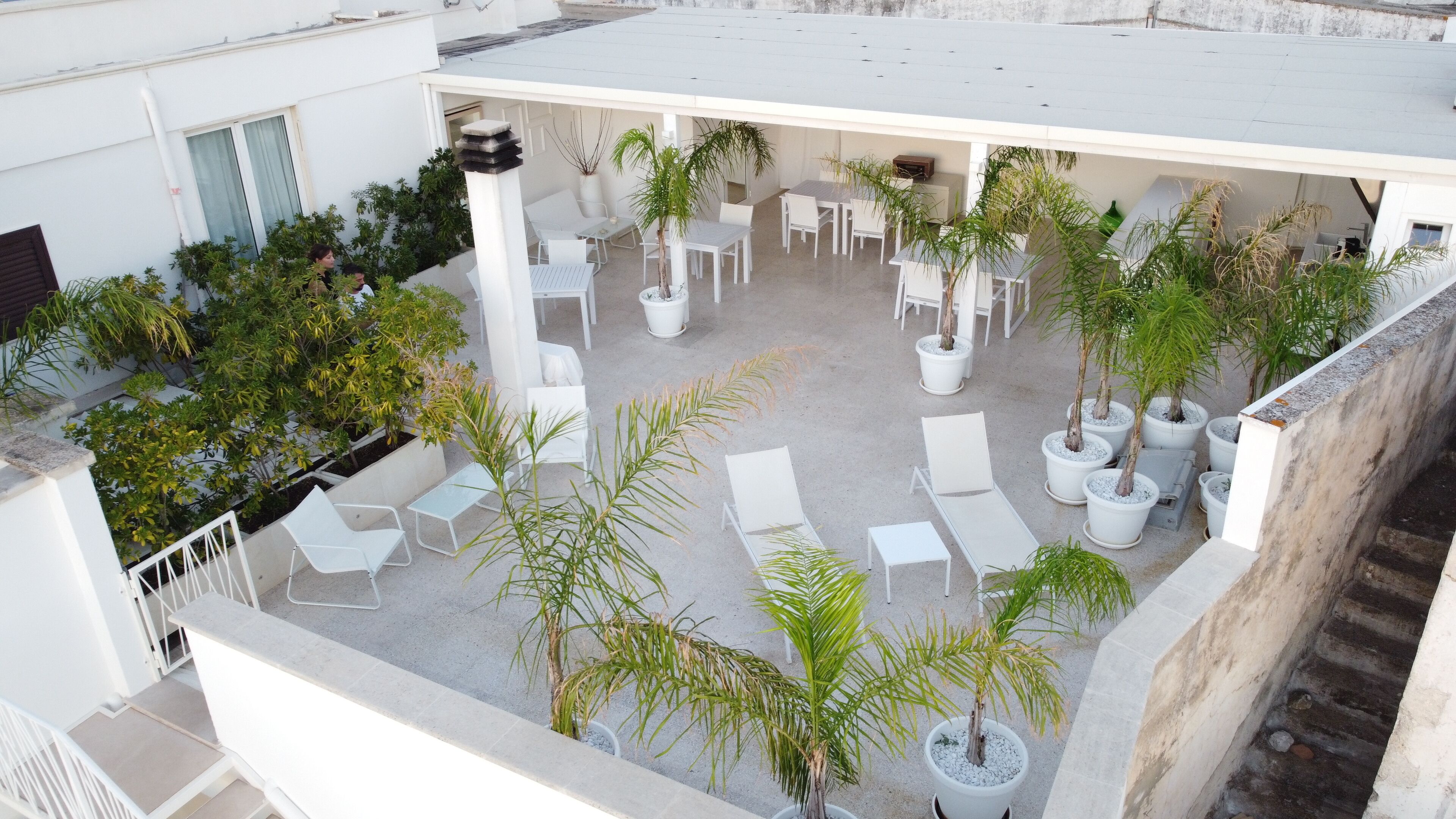 Una terraza en la azotea con sillones blancos, plantas en macetas y un área de estar con mesas y sillas.