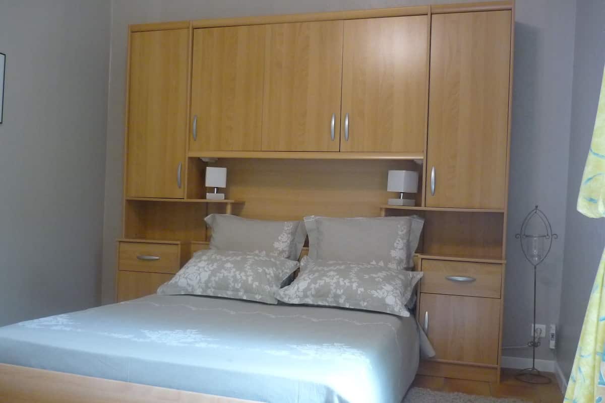 A bedroom with a bed, wooden wardrobe, bedside tables, and a floor lamp.
