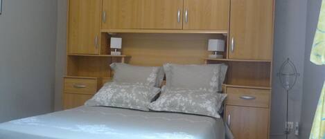 A bedroom with a bed, wooden wardrobe, bedside tables, and a floor lamp.