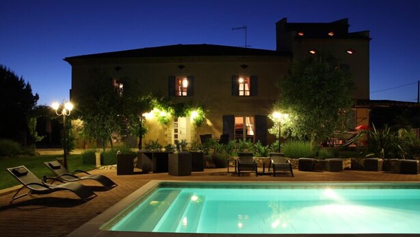 Une piscine avec des chaises longues, un bâtiment doté de nombreuses fenêtres et un éclairage extérieur.