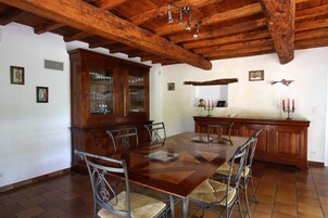 Un comedor con mesa y sillas de madera, un armario con cristalería y un techo con vigas a la vista.