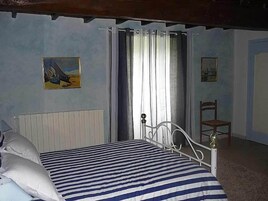 Un dormitorio con cama, una silla, un radiador y dos cuadros en la pared.