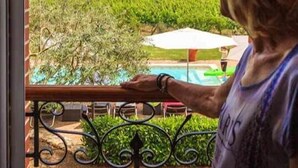 Une personne se tient près d’une fenêtre donnant sur un vignoble et une piscine.
