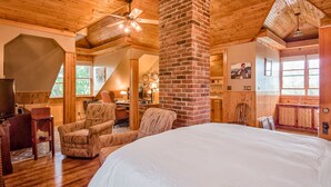 Un dormitorio amplio con una cama grande, techo de madera y chimenea de ladrillo.