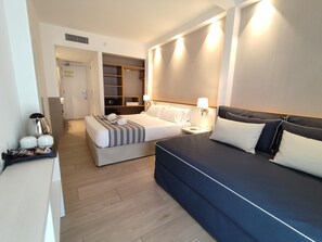 Une chambre d’hôtel avec un grand lit, un lit plus petit, un canapé, un bureau avec une bouilloire et une armoire.