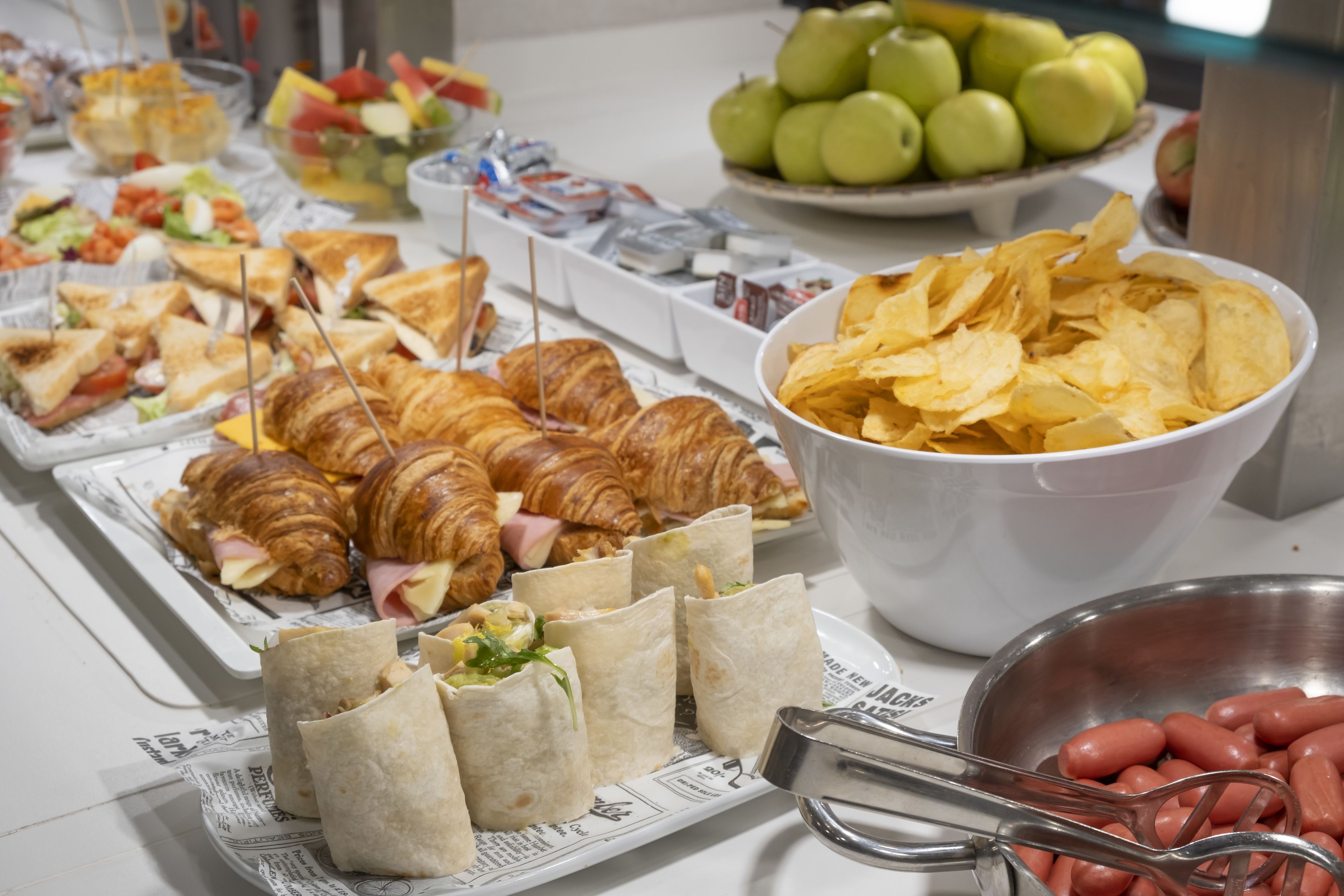 Un buffet proposant une variété de plats, notamment des sandwichs, des croissants et des chips.
