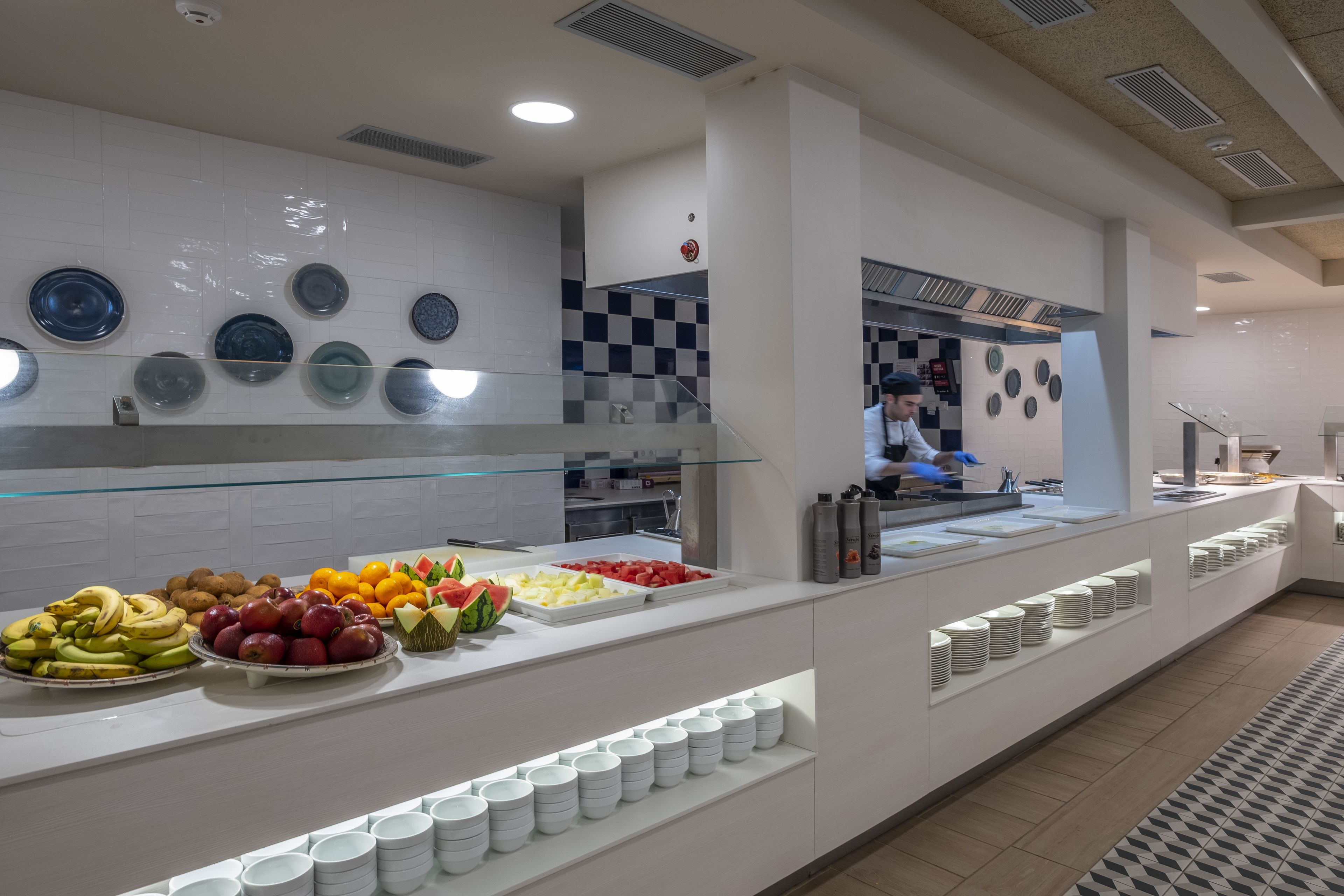 Ein Buffetbereich mit verschiedenen Früchten und Gemüsesorten, einer Glasvitrine und einer Anrichte mit Tellern und Beilagen.