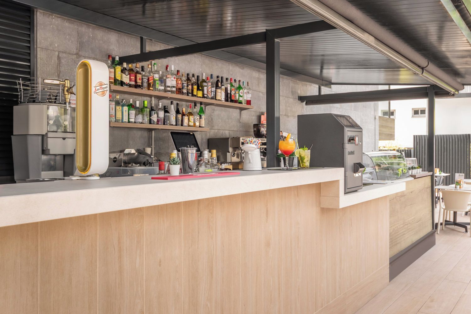 Un espace bar moderne comprenant un comptoir, des étagères remplies de bouteilles d’alcool, une machine à café et une grande machine à expresso.