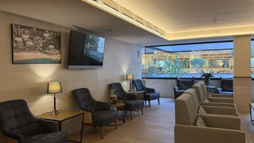 Eine Hotellobby mit einem Flachbildfernseher, einem großen Stadtbildgemälde und einer Sitzecke mit mehreren Stühlen und Tischen.