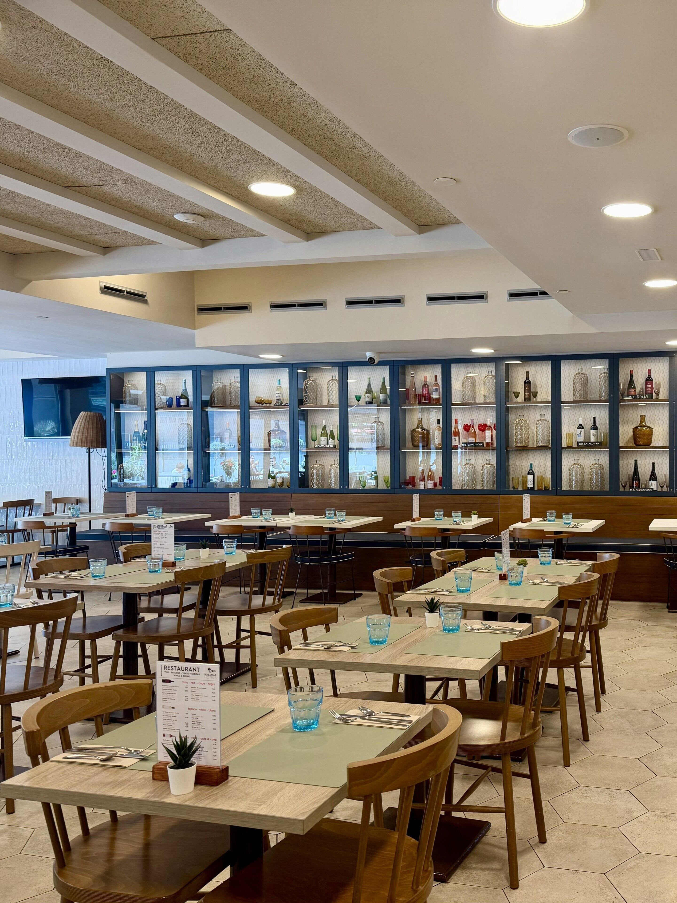 Un restaurante con varias mesas y sillas, un soporte para el menú y una exhibición de botellas detrás del mostrador.