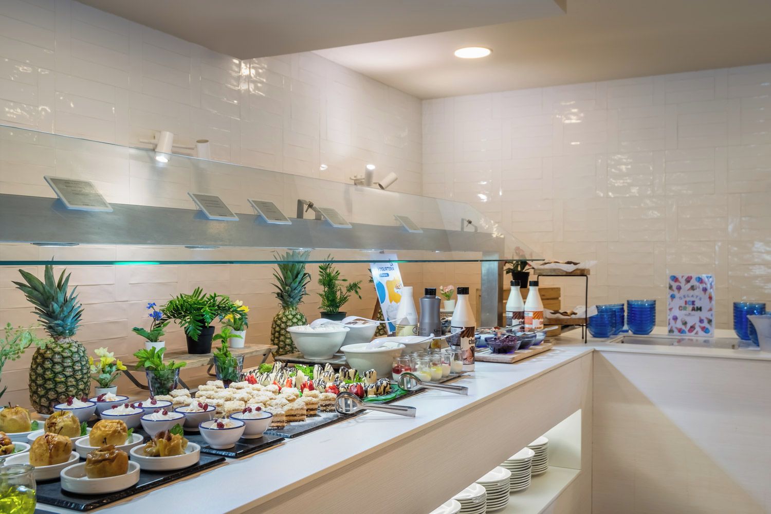 A buffet setup with various food items and beverages, including tropical fruits and desserts, in a modern hotel setting.