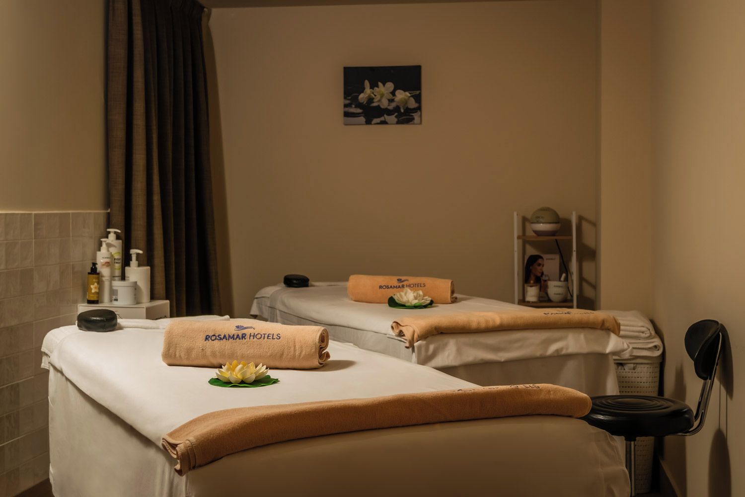 Une salle de spa équipée de deux tables de massage, de serviettes et d’une petite étagère contenant des articles de toilette.