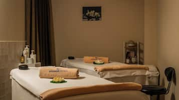 Une salle de spa équipée de deux tables de massage, de serviettes et d’une petite étagère contenant des articles de toilette.