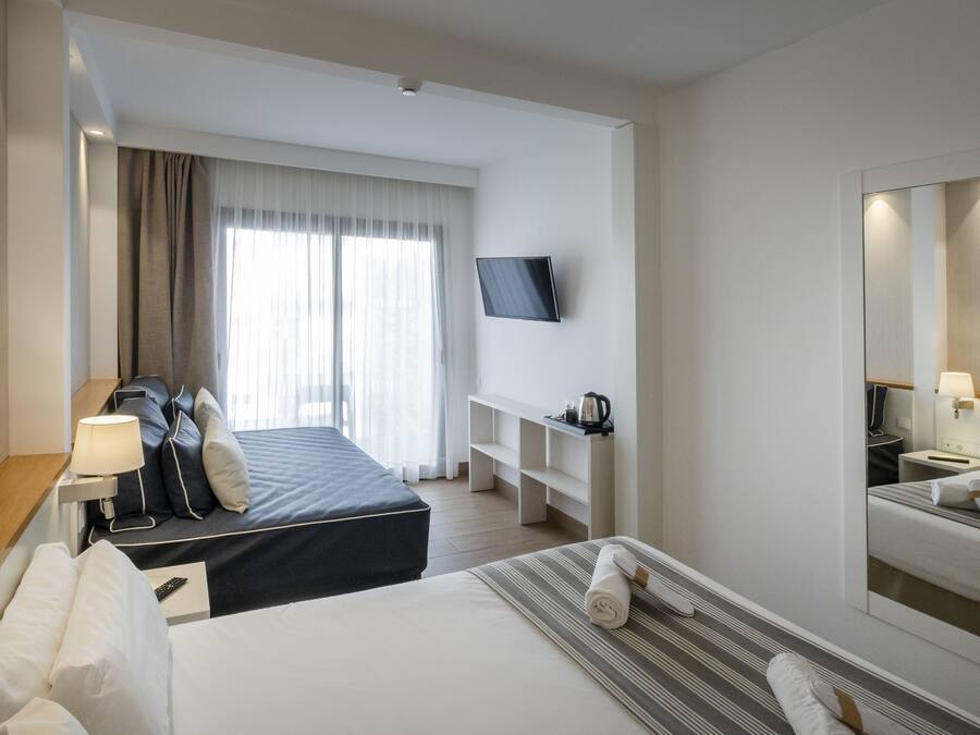 Hotelkamer met een bed, een bureau met lamp, een televisie, een nachtkastje met lamp, een spiegel en een raam met gordijnen.