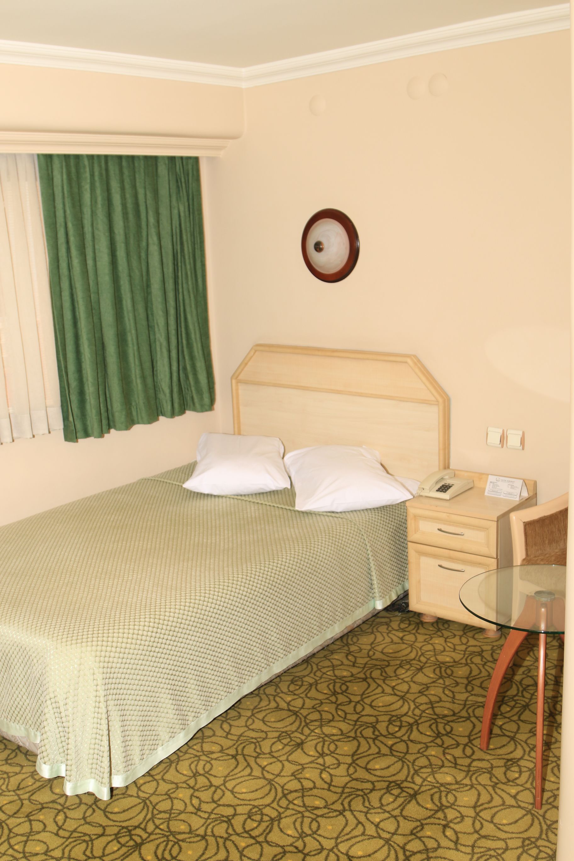 A hotel room with a single bed, a bedside table with a telephone, and a small glass table.