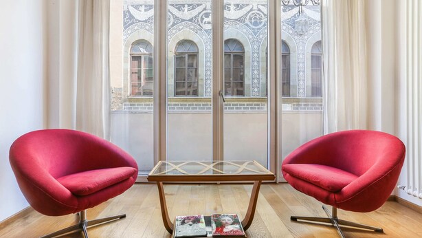 Une pièce avec deux chaises rouges, une table dont le plateau est en verre et un magazine posé sur le sol.