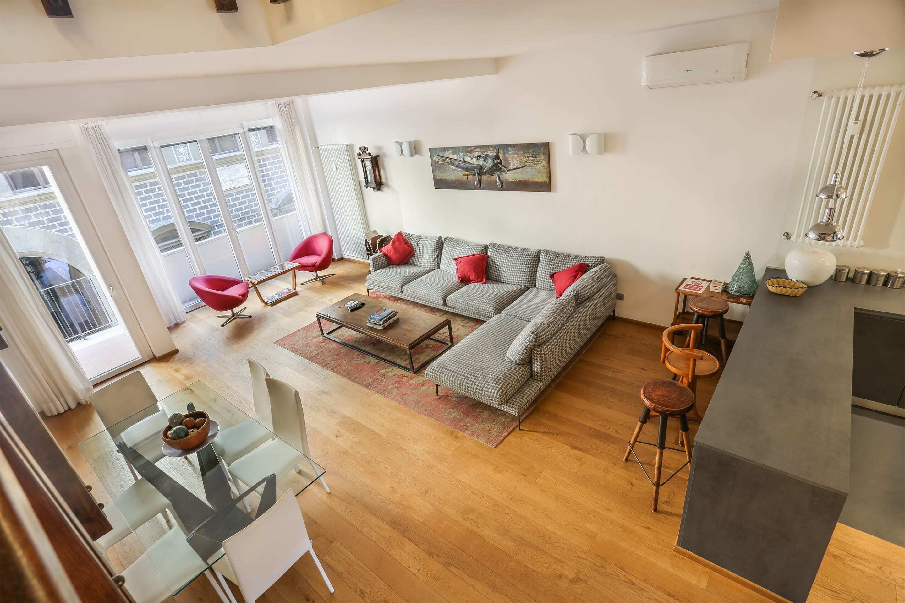 A spacious living area with a sofa, red chairs, a glass coffee table, and a dining table with chairs.