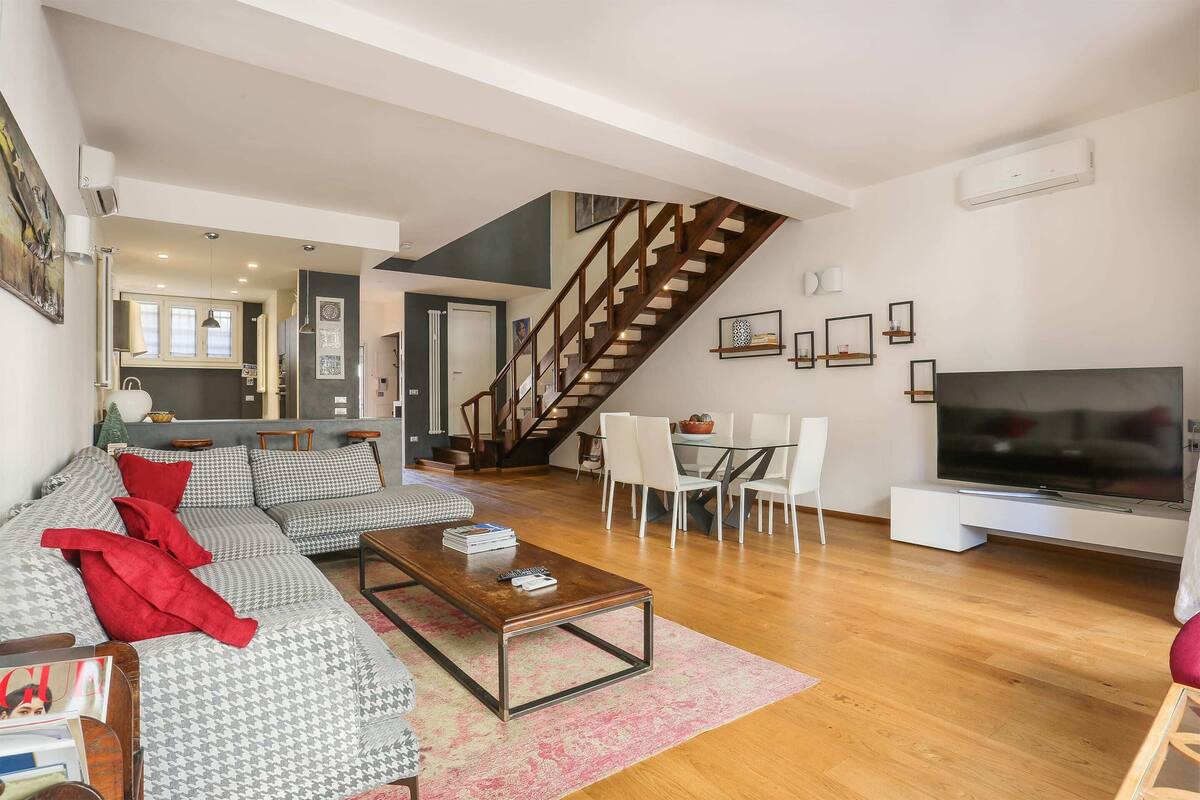 Een moderne woonkamer met een bank, salontafel en een televisie. Een trap leidt naar een andere kamer.