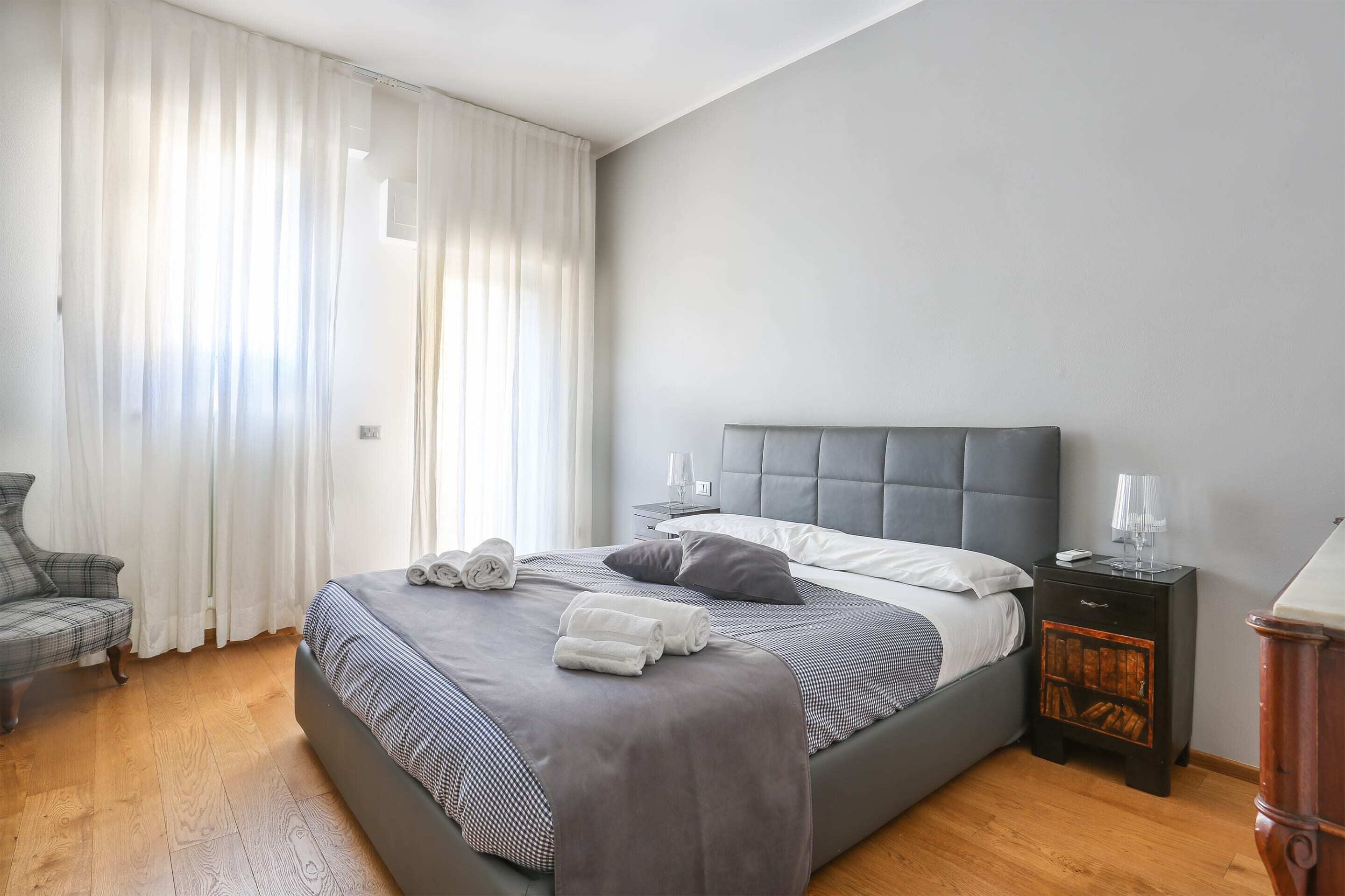 A bedroom with a bed, a chair, a nightstand, and a window with curtains.