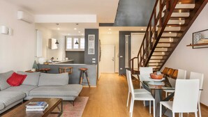 Un espace de vie moderne comprenant un canapé, une table à manger et des chaises. Un escalier mène à l’étage supérieur.